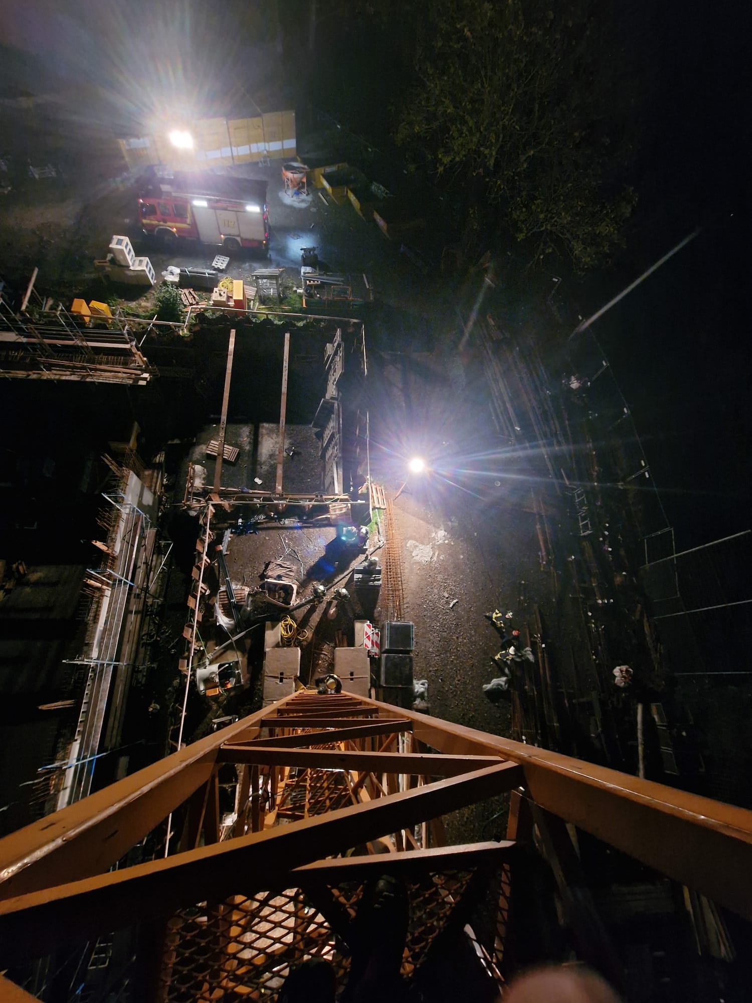 Blick aus großer Höhe herab von einem Baukran bei Nacht auf eine beleuchtete Baustelle