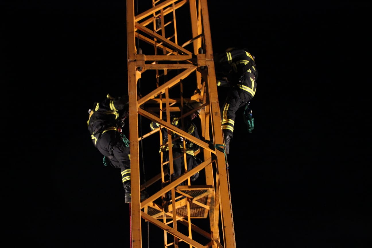 zwei Feuerwehrleute klettern bei Nacht auf einen Baukran