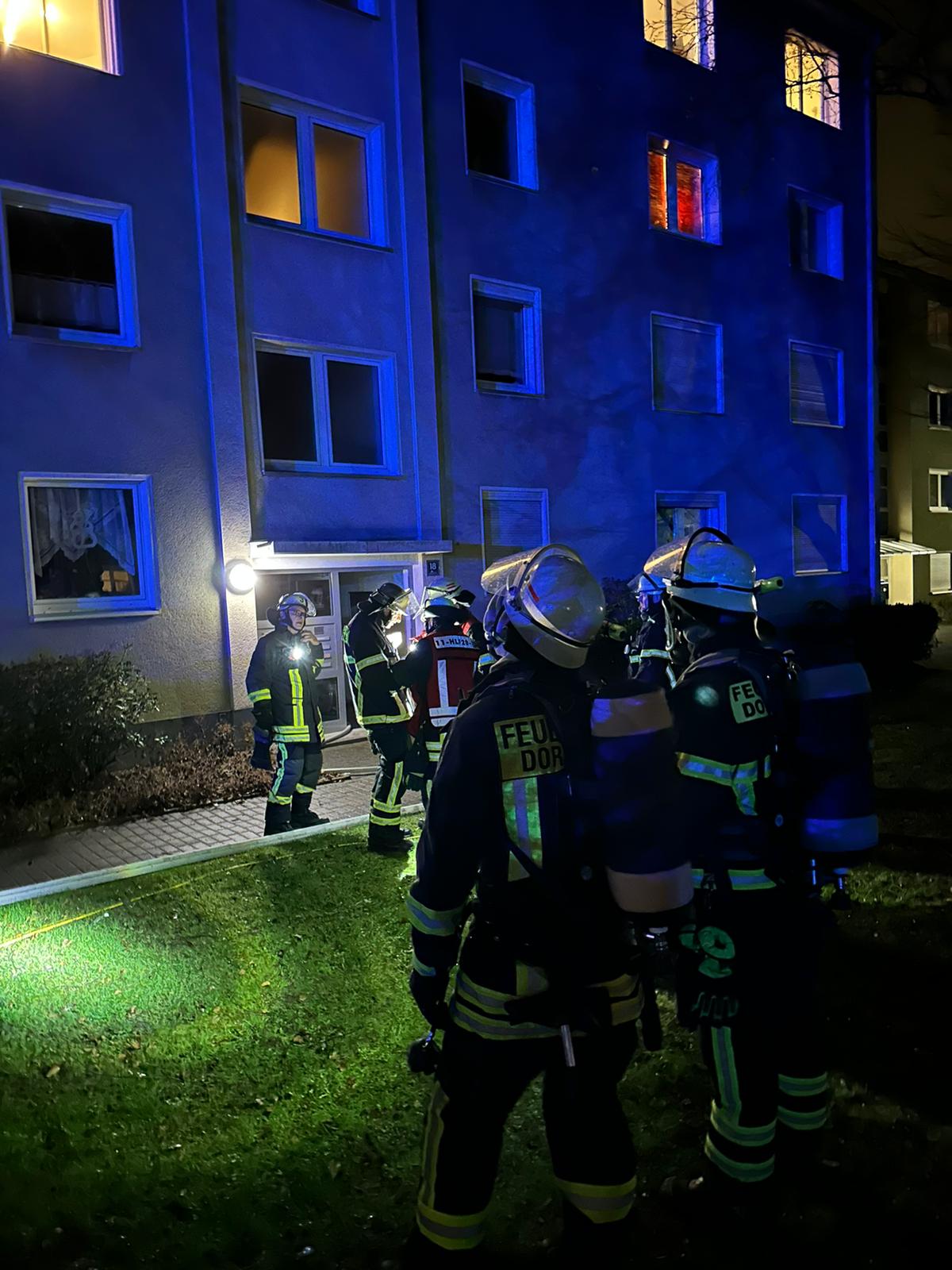 Feuerwehrleute stehen vor einem Mehrfamilienhaus im Bereitstellung