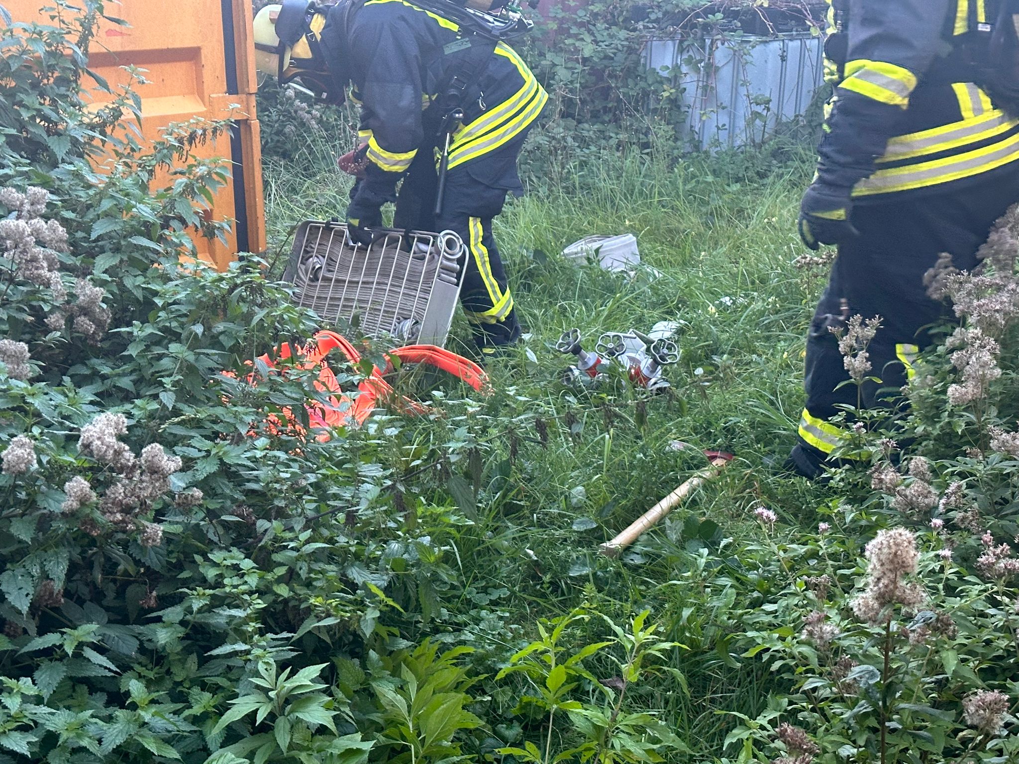 Feuerwehrleute verlegen Schlauchmaterial im Dickicht einer unzugänglichen Gebäuderückseite